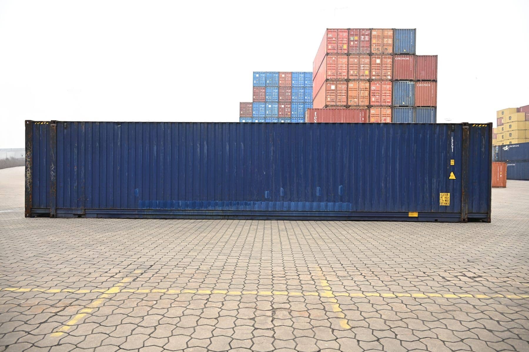Ein blauer 45 Fuß Container steht quer vor gestapelten Containern